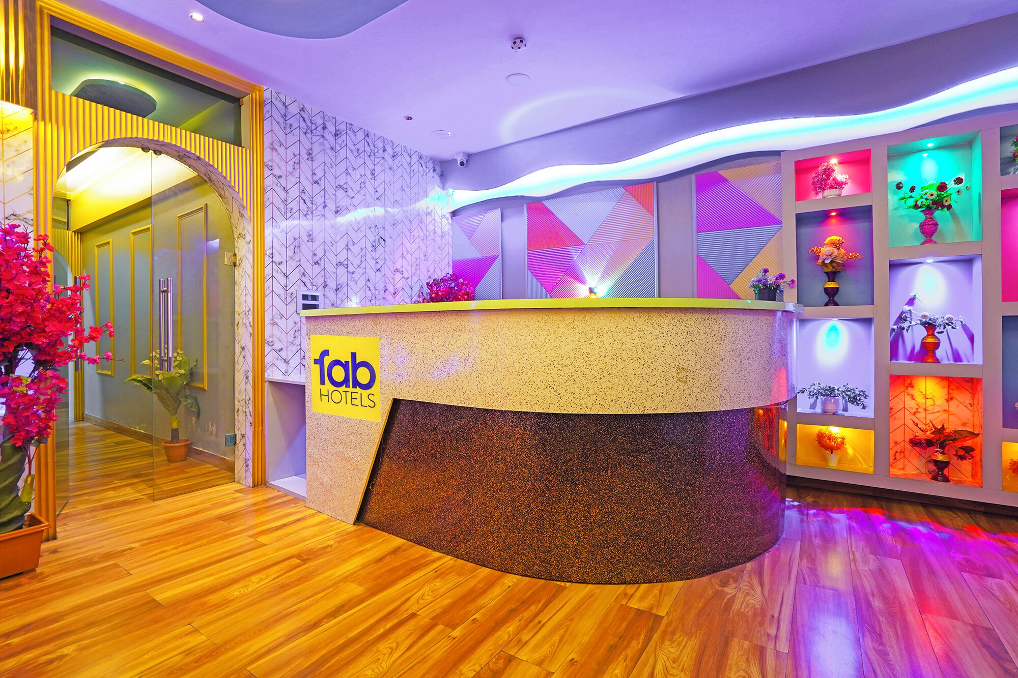 Zona de recepción de hotel con mostrador curvo, pared de mármol con diseño geométrico y suelo de madera.