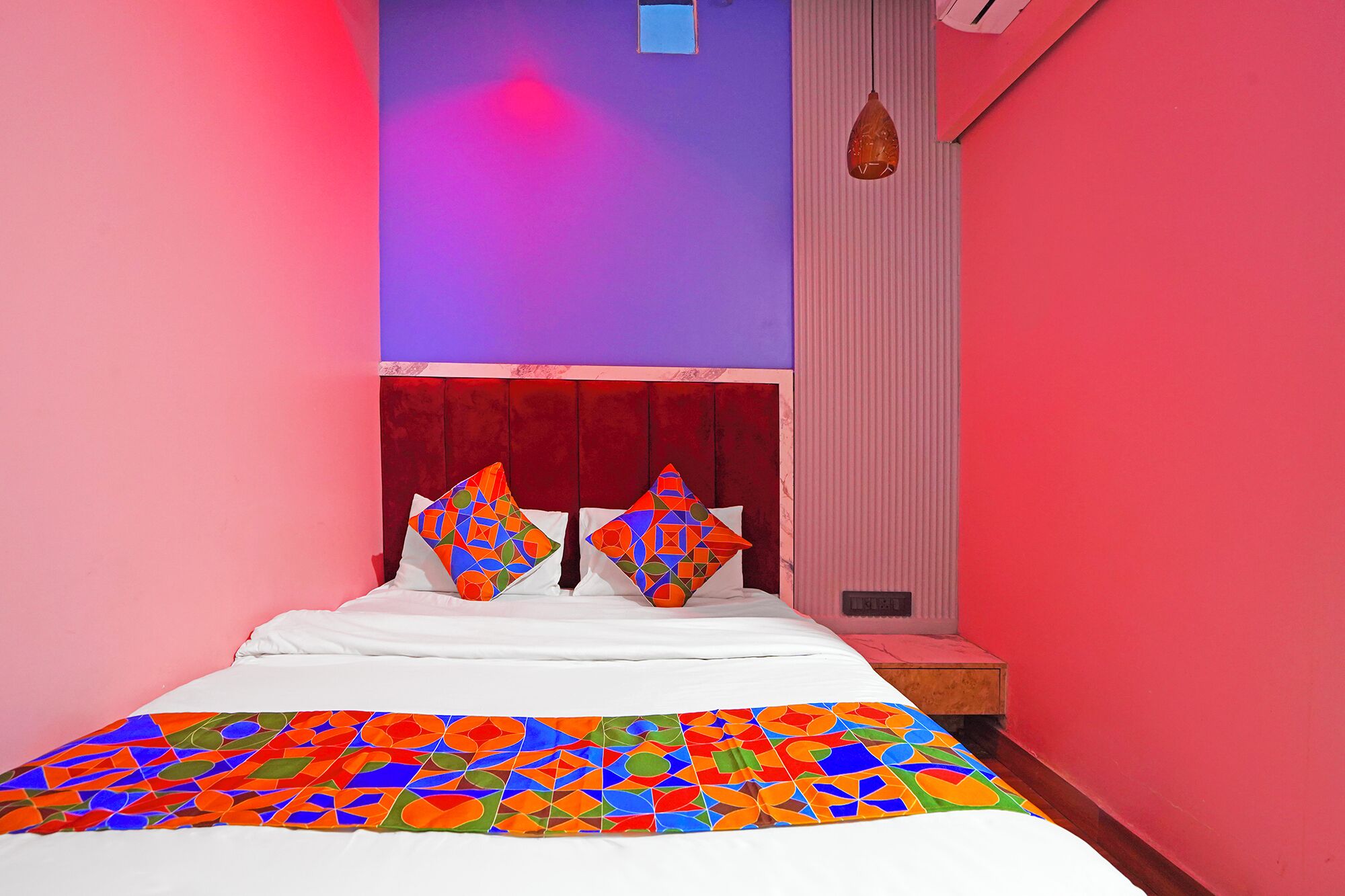 A bed with a colorful quilt, a red headboard, and a small bedside table with a lamp.