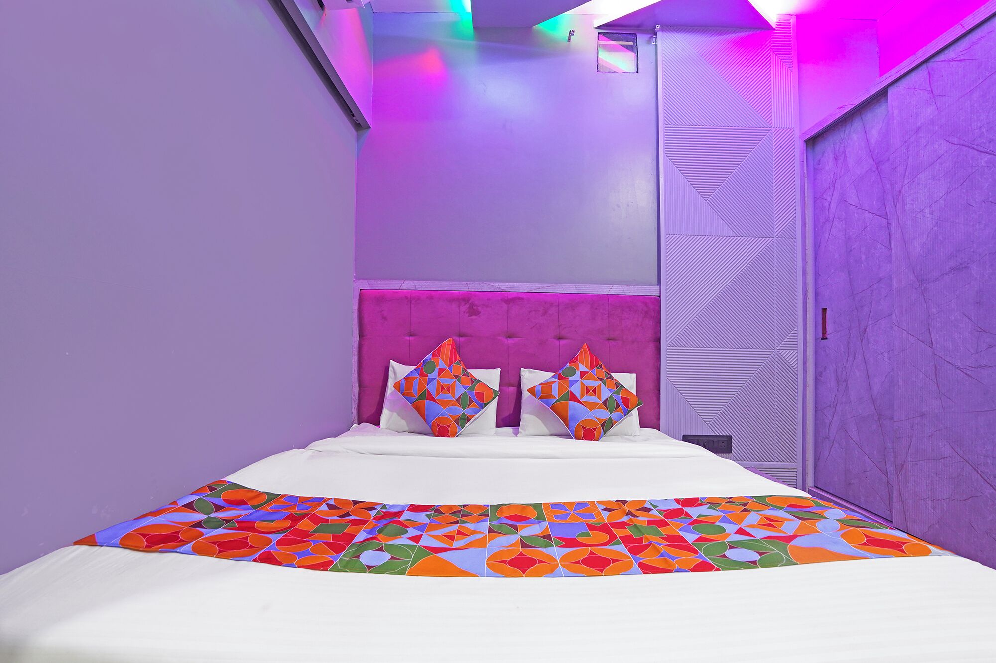 Ein Schlafzimmer mit einem Bett, zwei Kissen, einer gemusterten Tagesdecke und einer Tür mit geometrischem Dekor.
