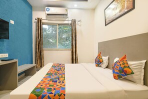 A hotel room with a bed, a TV, an air conditioner, and a window with curtains.