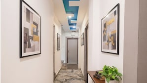 A hallway with framed artwork on the walls, a marble floor, and a table with a plant. - Fabhotel Bine Venue (Bhopal)