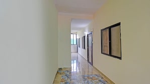 A hallway with a marble floor, white walls, and framed pictures on the right. - Fabhotel Shree Sai Inn (Paud)