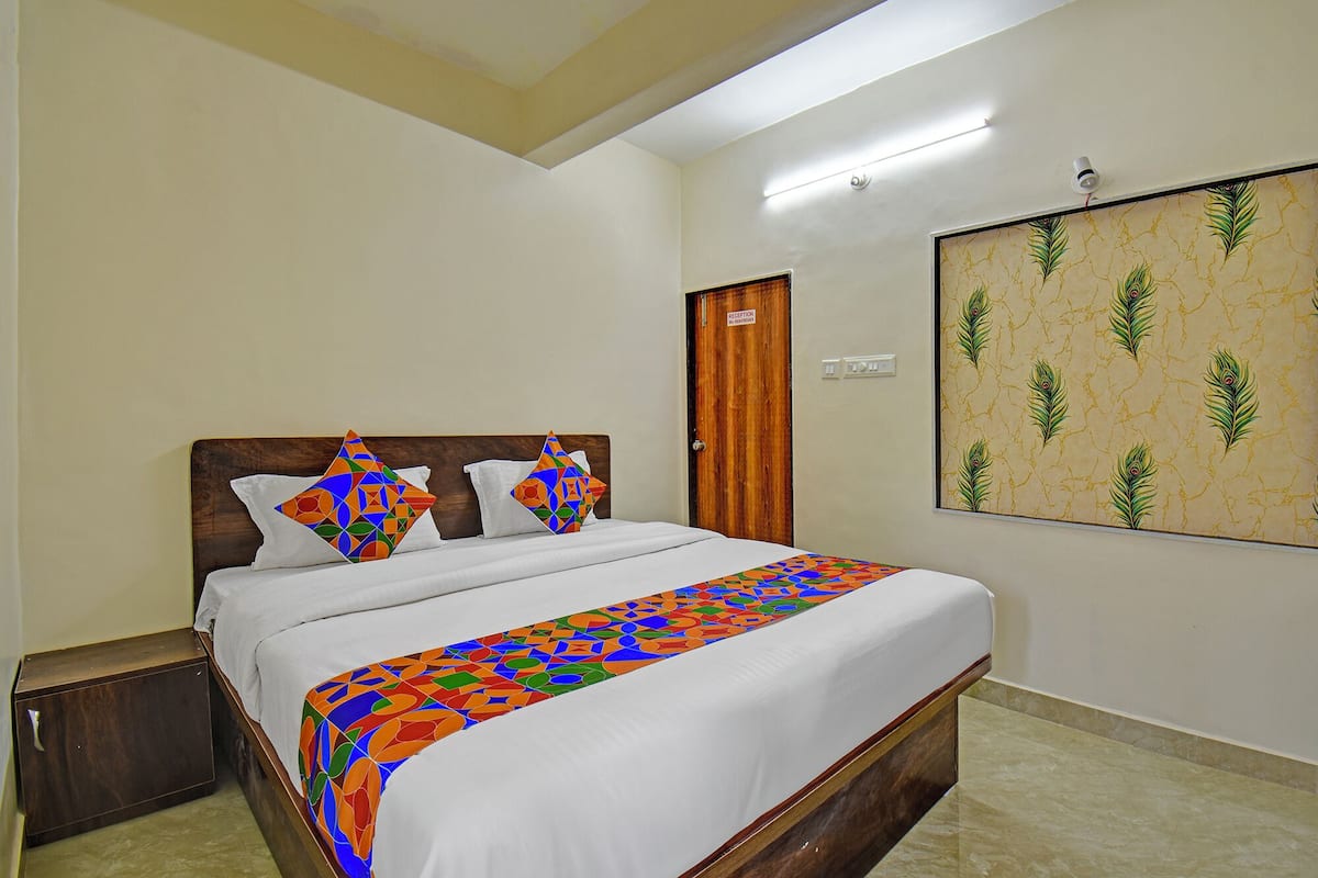 Quarto de hotel com cama, mesa de cabeceira, porta de recepção e parede com padrão de pena de pavão.