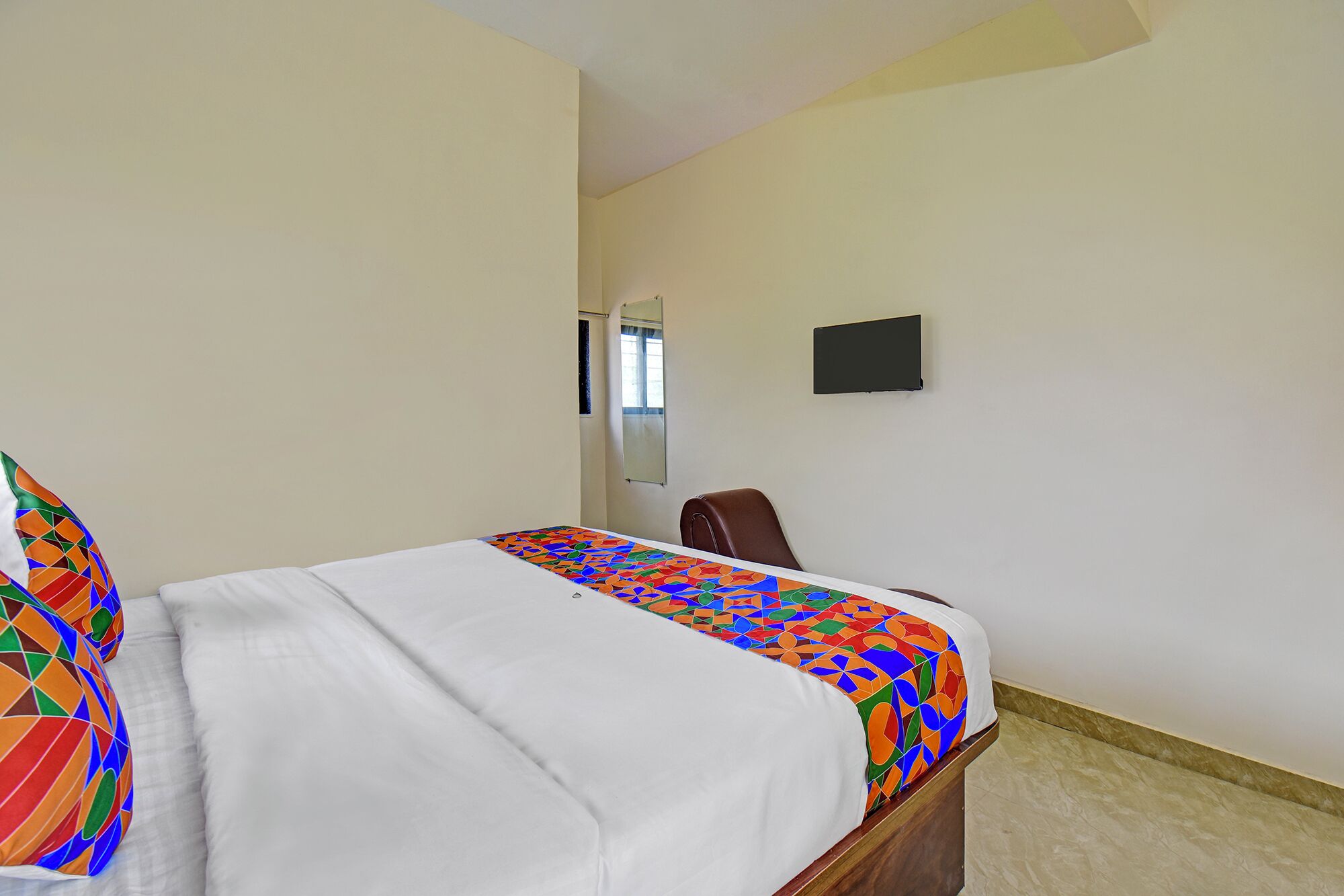 A hotel room with a bed, a chair, a TV, and a window.