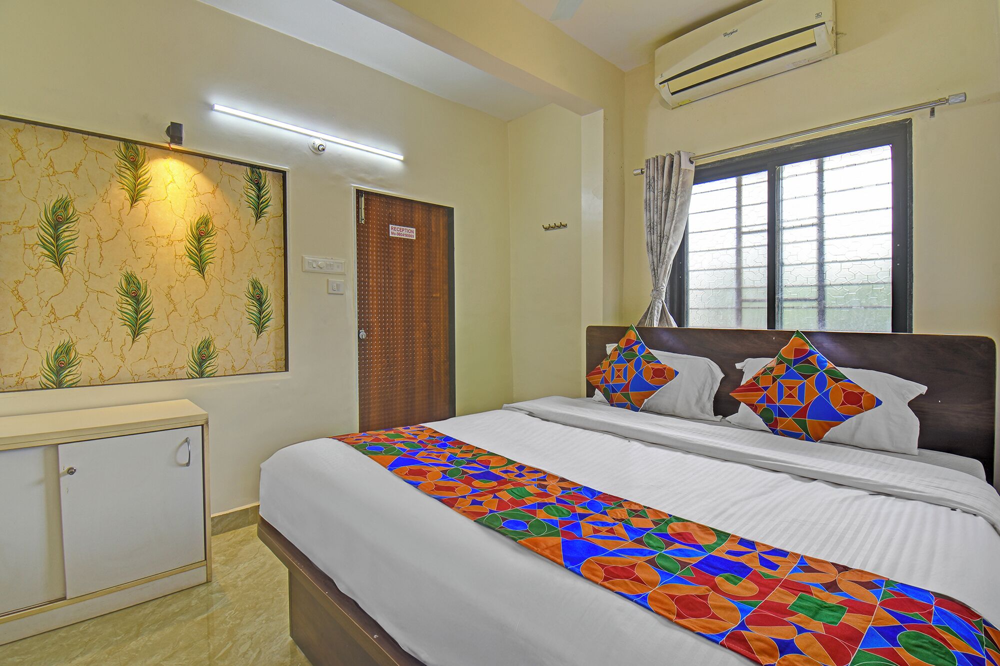 A hotel room with a bed, a reception area, and a window with curtains.