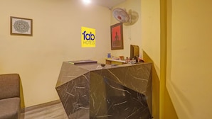 Un comptoir d’accueil d’hôtel avec un plateau en marbre, une statue de Bouddha encadrée, un ventilateur et un panneau indiquant « Tab Hotels ».