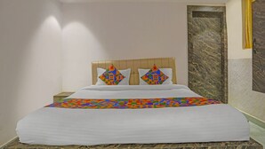 Un lit bien fait, avec une couette blanche et des coussins aux motifs géométriques et aux couleurs vives.