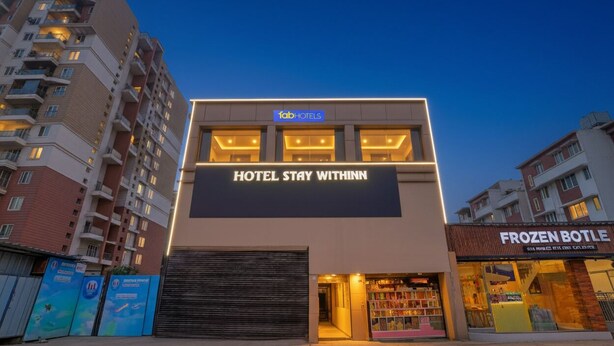 Un hôtel moderne avec une enseigne indiquant « HOTEL STAY WITHINN » et une boutique appelée « FROZEN BOTTLE » située juste à côté.
