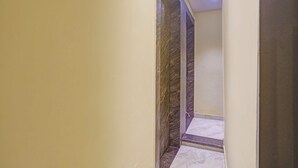 Un couloir étroit avec un mur de marbre et une petite marche menant à une porte.