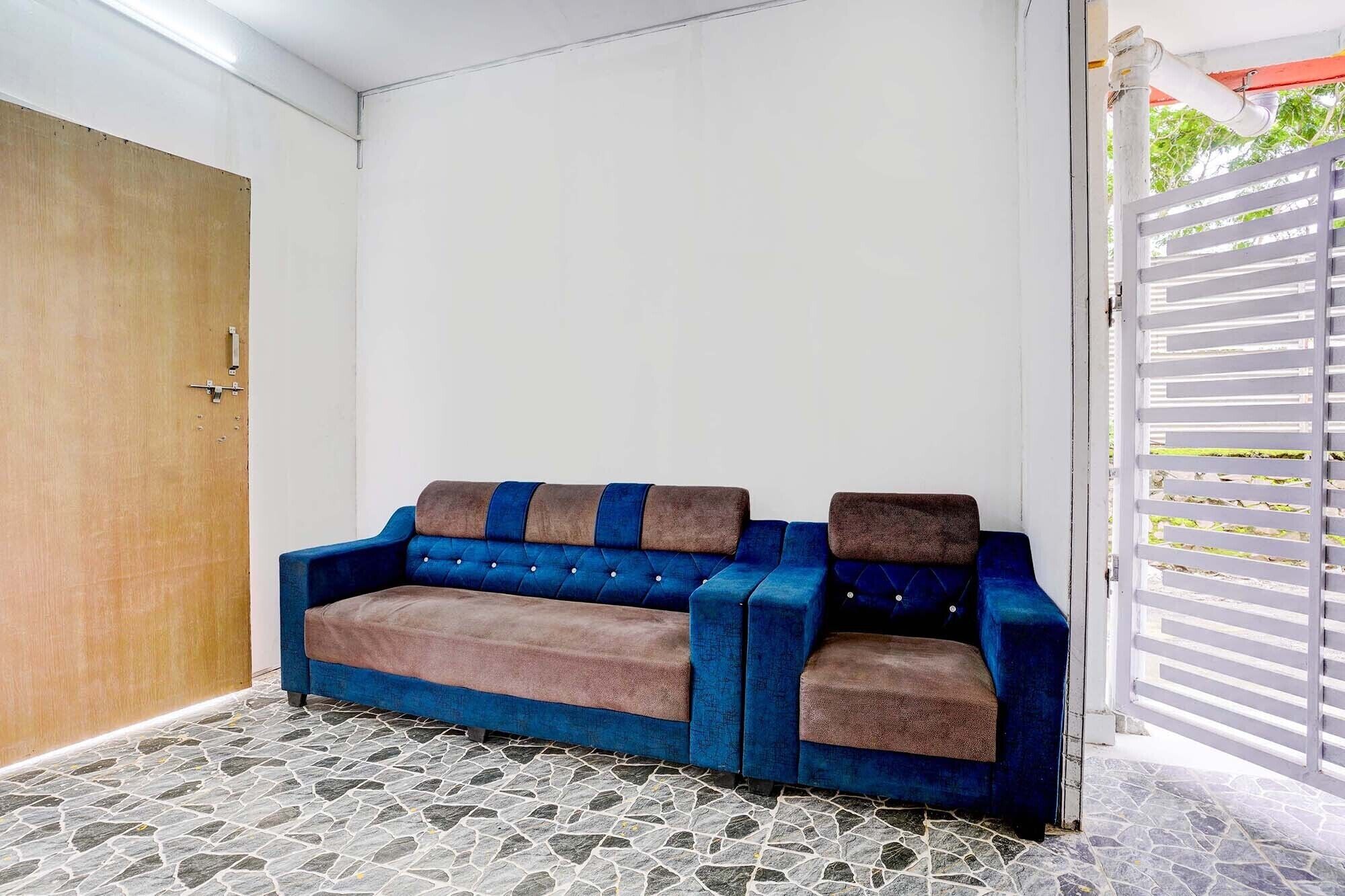 A blue sofa with brown cushions in a room with a stone-tiled floor and a wooden door.