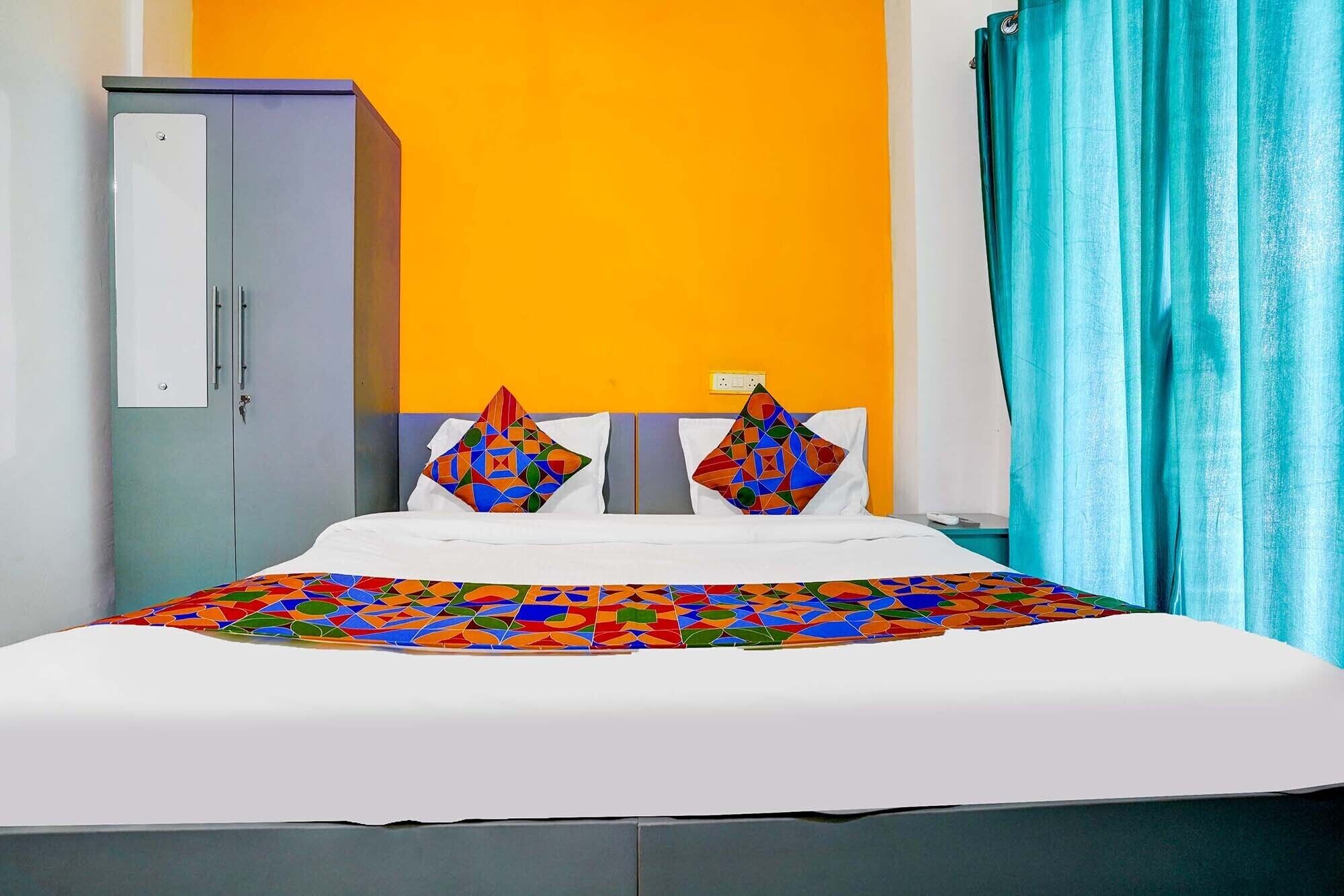 A bed with a colorful geometric-patterned bedspread, two decorative pillows, a white headboard, and a grey wardrobe against a yellow wall.