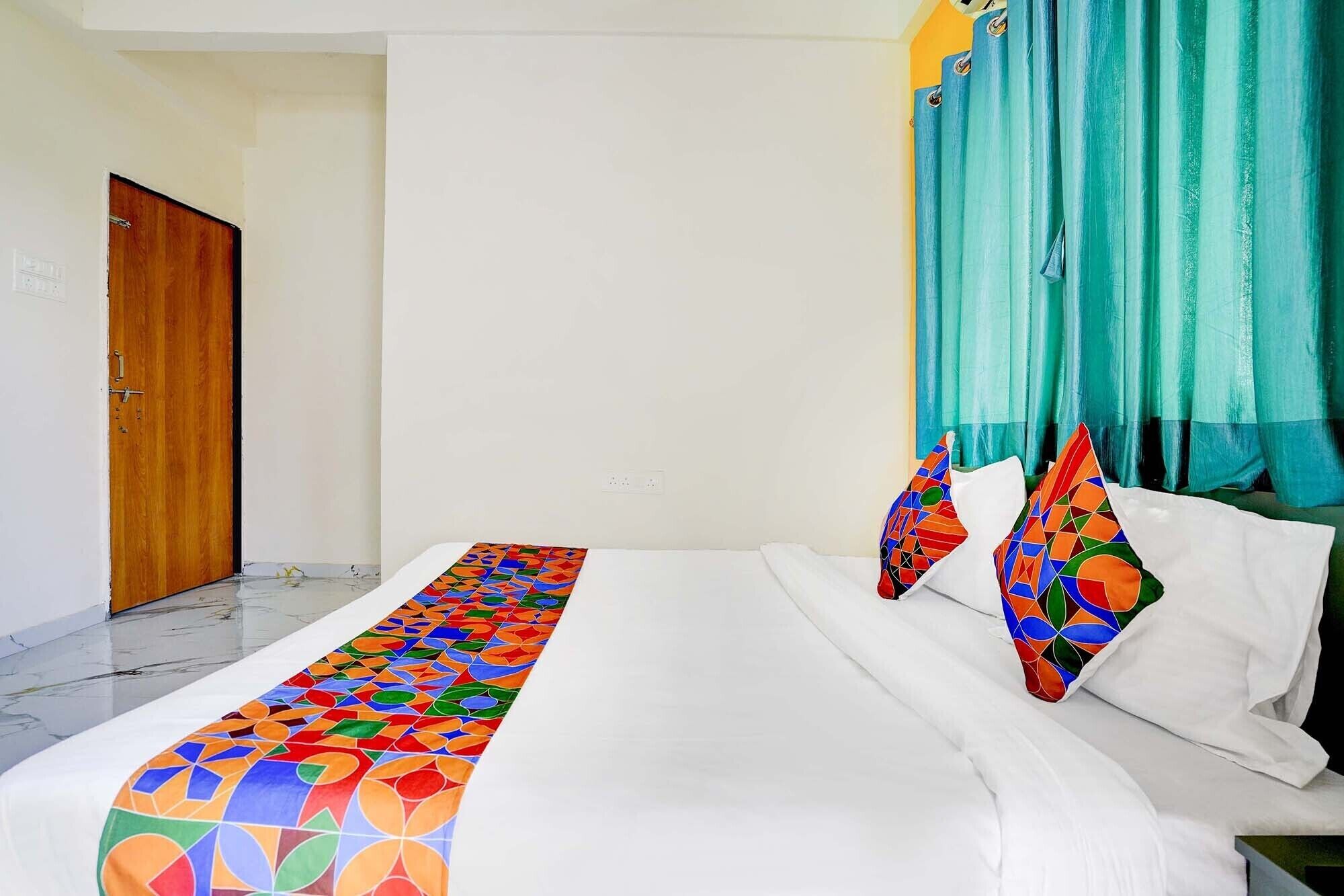 A hotel room with a bed, white curtains, and a colorful bedspread.
