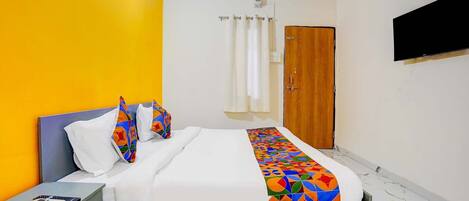 A hotel room with a bed, a nightstand, a wooden door, and a TV mounted on the wall.