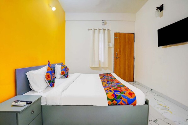 A hotel room with a bed, a nightstand, a wooden door, and a TV mounted on the wall. - FabHotel Lotus Prime Stay - Hinjawadi (Paud)