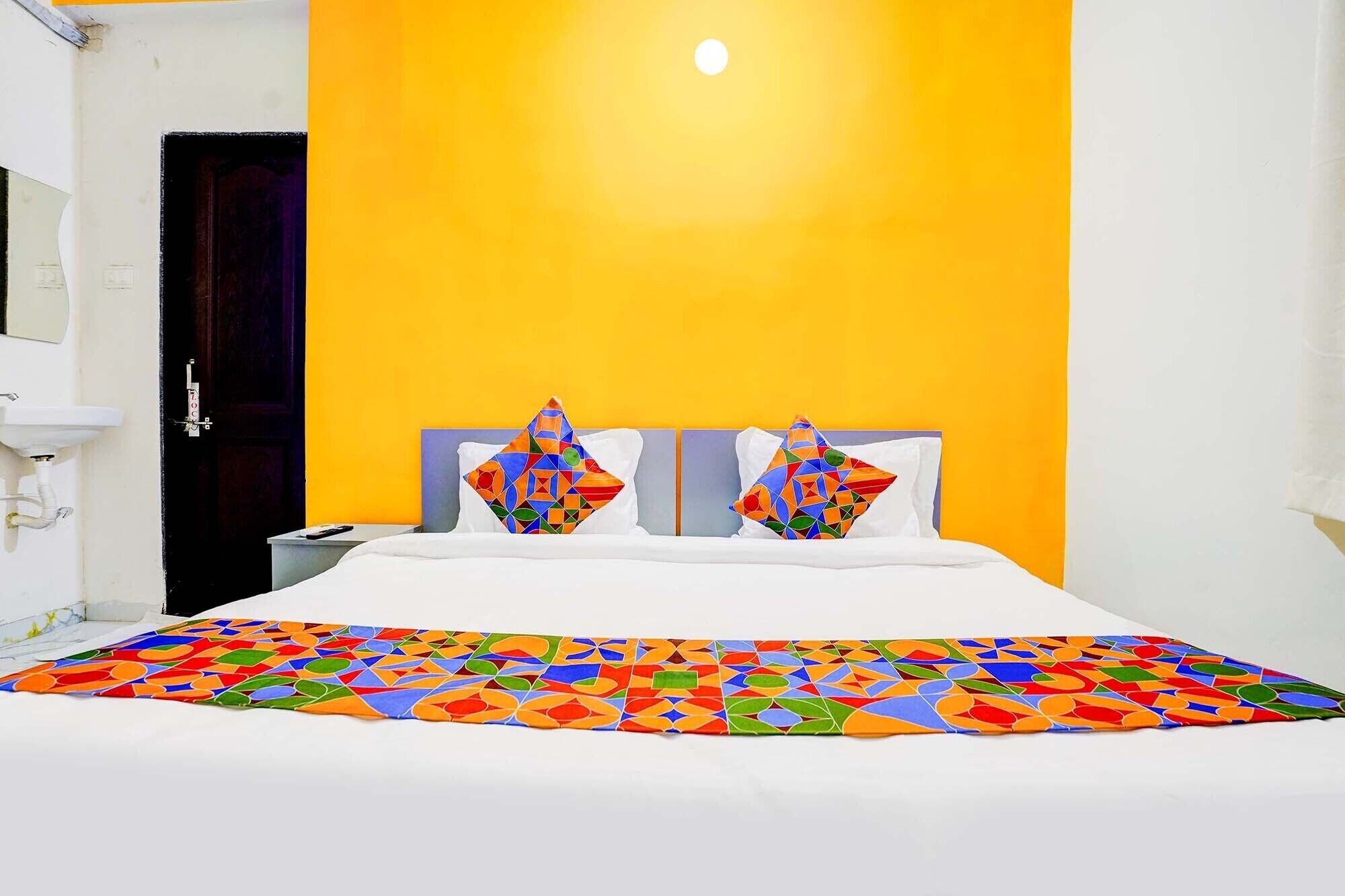 Habitación de hotel con cama, dos almohadas de diseños geométricos, mesita de noche y lavamanos blanco.