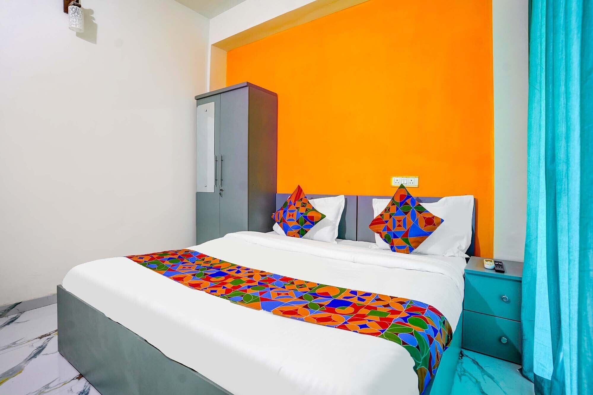Habitació d'hotel amb llit, una tauleta de nit, armari i un edredó amb un disseny geomètric i colorit.