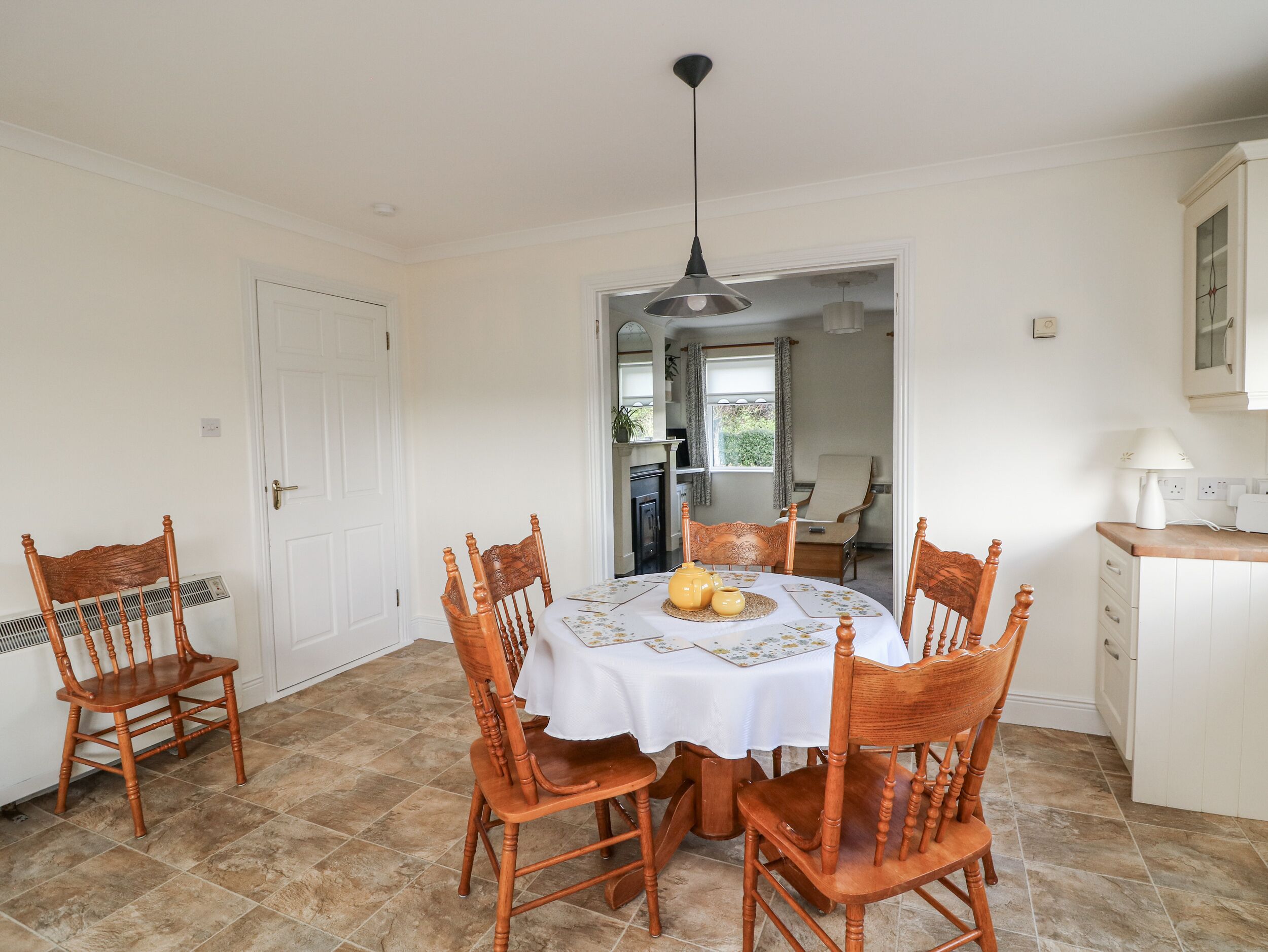A dining area with a round table, six wooden chairs, a white tablecloth, and a hanging pendant light.