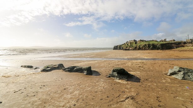 A beach with rocks in the foreground and a grassy cliff in the background.