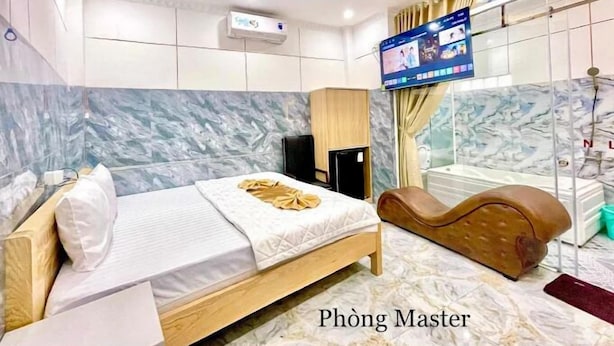 Habitación de hotel moderna con cama, sillón de masaje, televisor y pared de mármol.