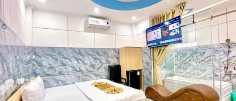 A modern hotel room with a bed, a massage chair, a TV, and a marble wall.