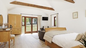 Un dormitorio con una cama de madera, un escritorio con silla, un televisor y un amplio ventanal corredero que da a un espacio exterior.