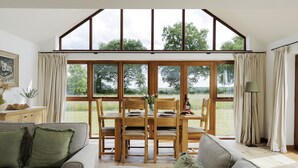 Comedor con una mesa lista para cuatro, sillas de madera y vista a un campo verde a través de amplios ventanales.