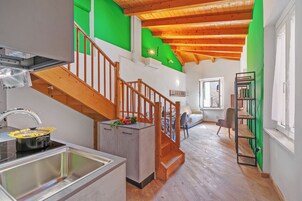 A modern kitchen with a wooden staircase, a dining area, and a green accent wall.