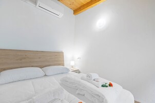 A hotel room with a wooden headboard, white bedding, a bedside table with a lamp, and a small bouquet of flowers.
