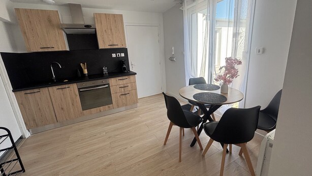 Et moderne køkken med træskabe, en sort bordplade og et spiseområde med et rundt bord og sorte stole.