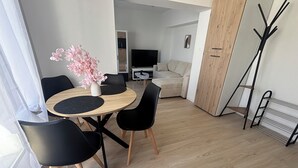 En moderne stue med et rundt træbord, sorte stole, en beige sofa, et fjernsyn og et knagered.