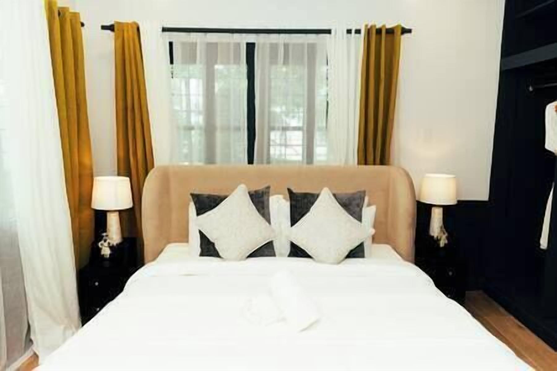 Een hotelkamer met een bed, twee bedlampen, een raam met gordijnen en een deur.