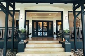 Entrada de hotel con una escalera que lleva a una puerta oscura, flanqueada por dos macetas.