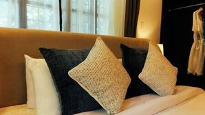 Una cama con cabecera color beige, dos almohadas oscuras y una almohada blanca.