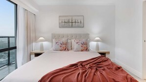 A modern bedroom with a large bed, two bedside lamps, a city view, and a framed artwork on the wall. - Stunning Views of Rangitoto Kitchen Gym Rooftop Pool Parking (Auckland)