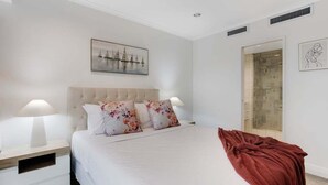A bedroom with a large bed, white bedding, a red throw blanket, and two bedside lamps. - Stunning Views of Rangitoto Kitchen Gym Rooftop Pool Parking (Auckland)