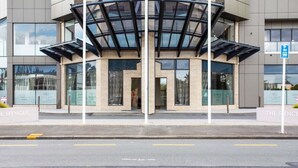 A modern building with a glass entrance and a covered area. - Stunning Views of Rangitoto Kitchen Gym Rooftop Pool Parking (Auckland)