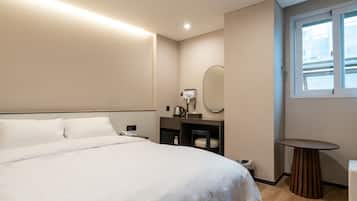 A hotel room with a large bed, a bedside table, a mirror, a small round table, and a window with blinds.