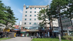 Un hotel con fachada moderna, entrada visible y zona de estacionamiento al frente.