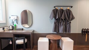 Un baño moderno con lavamanos, espejo, perchero para batas y una pequeña mesa con taburetes.