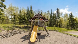Un terrain de jeux équipé d’un toboggan et de structures d’escalade, entouré d’arbres et recouvert de gravier.