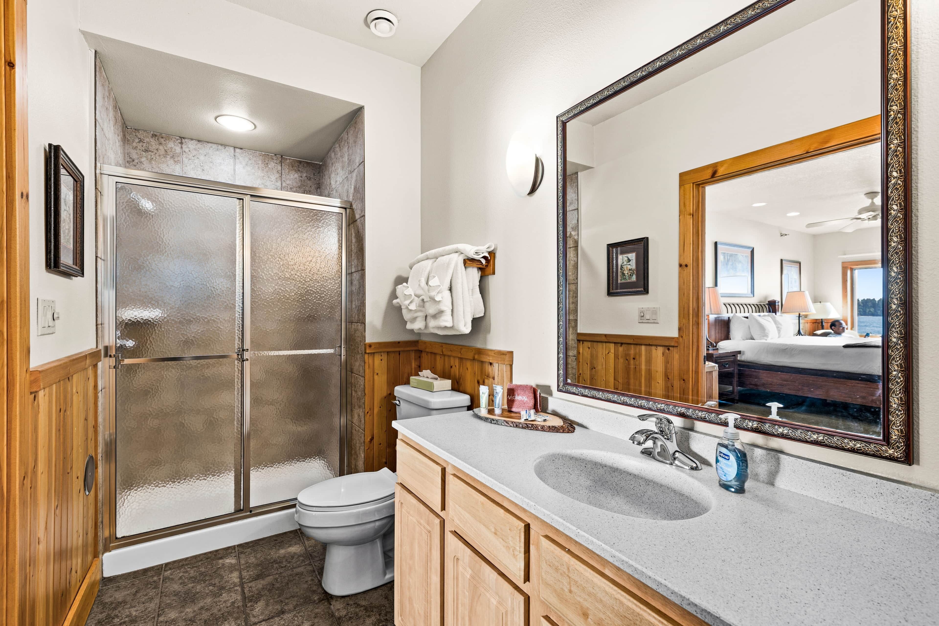 A bathroom with a glass shower enclosure, a toilet, a sink with a mirror, and wooden cabinets.