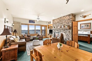 A spacious living area with a fireplace, a dining table, and a view of the outdoors. - Majestic Lake Views | 1BR w/King Suite | Pools (Two Harbors)