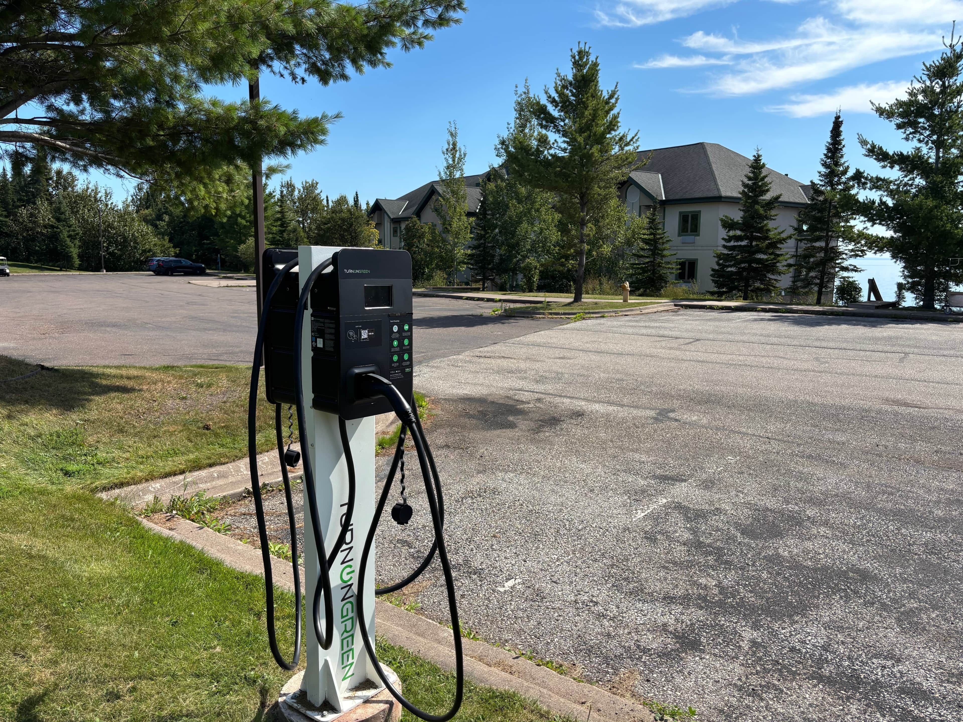 A parking area with a charging station labeled 'TURNINGGREEN' and a residential building in the background.