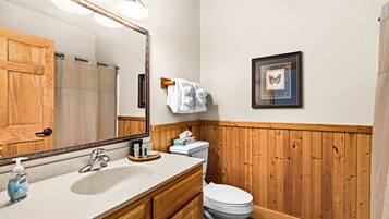 A bathroom with a wooden vanity, a sink, a toilet, and a mirror.
