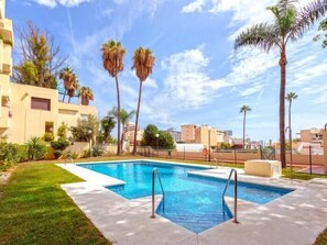 Une piscine à l’eau d’un bleu cristallin, entourée d’une pelouse bien entretenue et de palmiers.