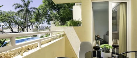 A balcony with a pool, chairs, and a table with wine glasses and magazines.