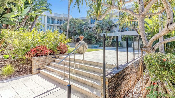 A staircase leading to a building with a modern design, surrounded by lush greenery and palm trees.