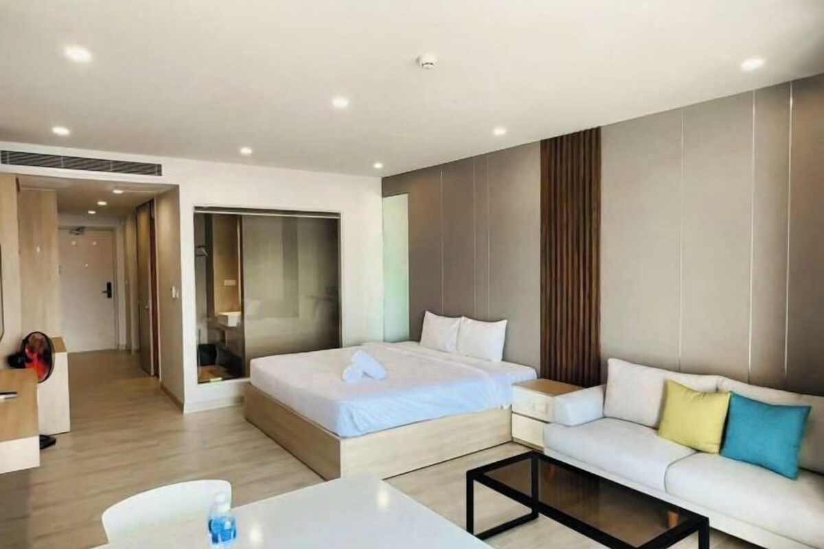 A modern hotel room with a large bed, a sofa, a coffee table, and a desk.