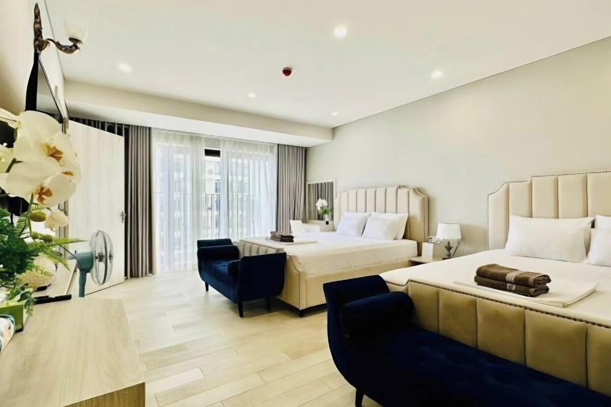 A hotel room with two beds, a desk, a chair, and a large window.