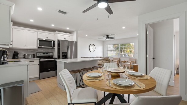 A modern kitchen with white cabinets, stainless steel appliances, and a dining area with a round table set for four. - 3BR Home • River Access • Boating • Screened Lanai (Fort Myers)